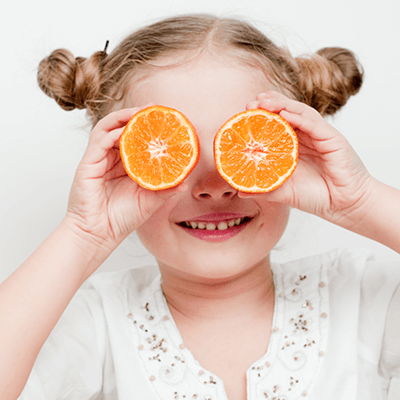 Picture of a child holding oranges over her eyes