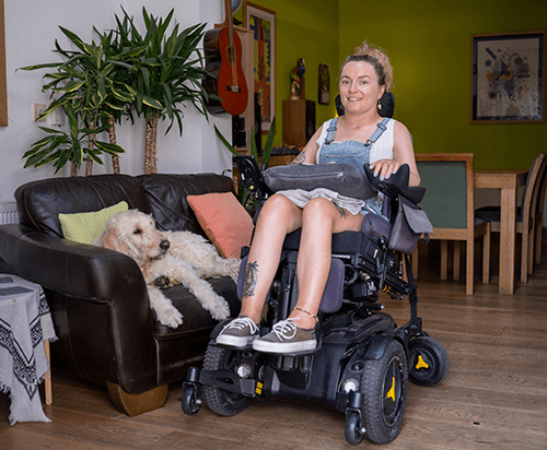Image of a woman in a wheelchair and a dog sitting down on a sofa