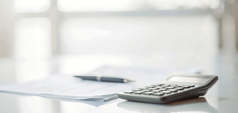 A calculator, pen and paper resting on a table