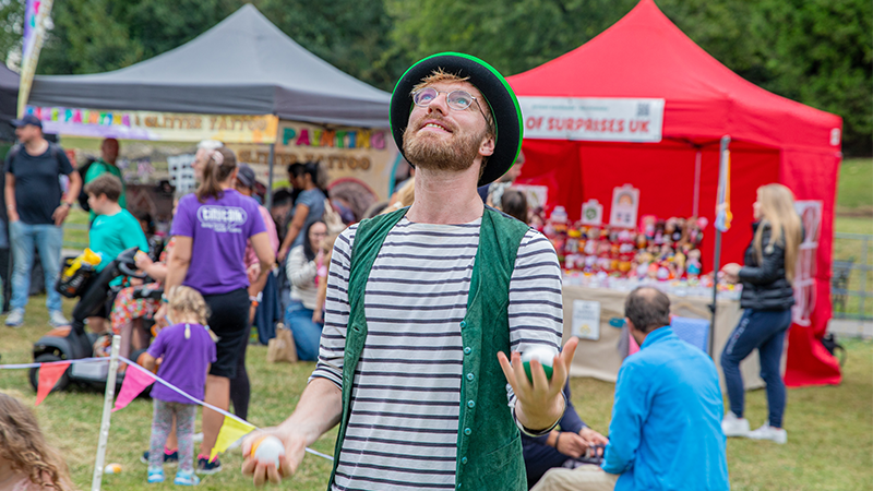 Juggler in a black hat and green waistcoat tossing balls at a festival