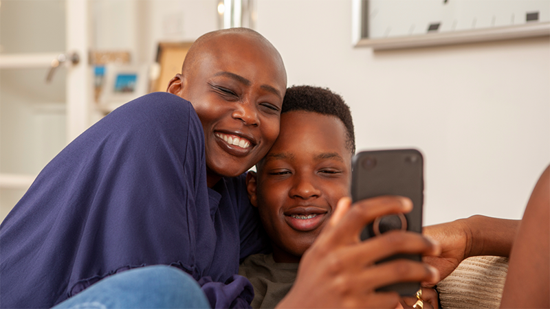 Two people sitting on a couch smiling at a phone