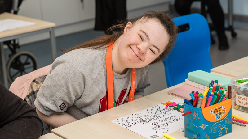 Student in classroom, smiling at the camera