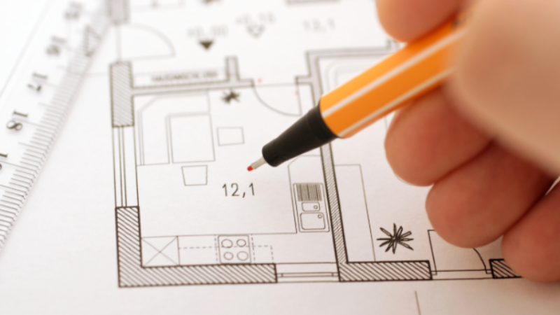 Hans holding a pen drawing a plan for a building