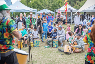 A group of people sitting on the grass with tents and drums
