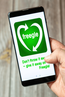 A hand holding a mobile phone displaying the Freegle app