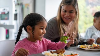 A young girl sitting with her foster family at the dining table
