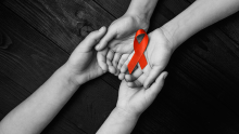 Image shows two people holding hands and a red ribbon to show support for World Aids Day